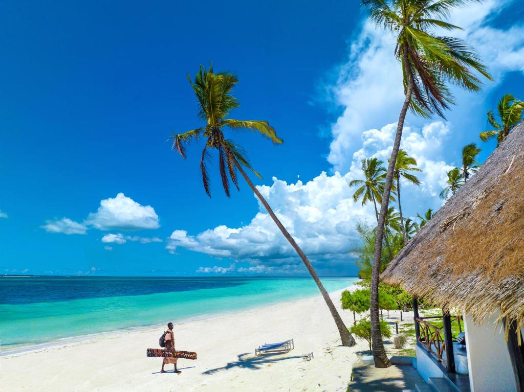 a man walking on a beach with a bench and palm trees at F-Zeen Boutique Hotel Zanzibar in Uroa