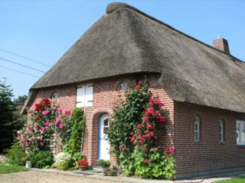 a brick house with a thatched roof with flowers at Friesenhof Mühlenwarft in Dagebüll