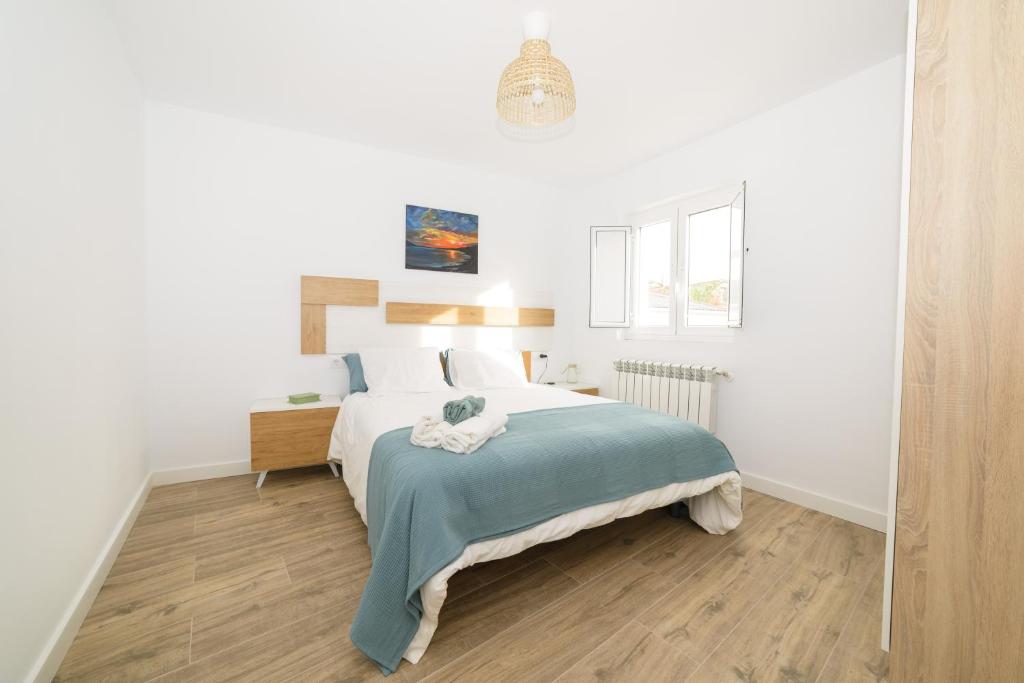een witte slaapkamer met een bed met een blauwe deken bij Apartamentos turísticos Praia de Seselle, terraza y jardín a un paso de la playa in Ares