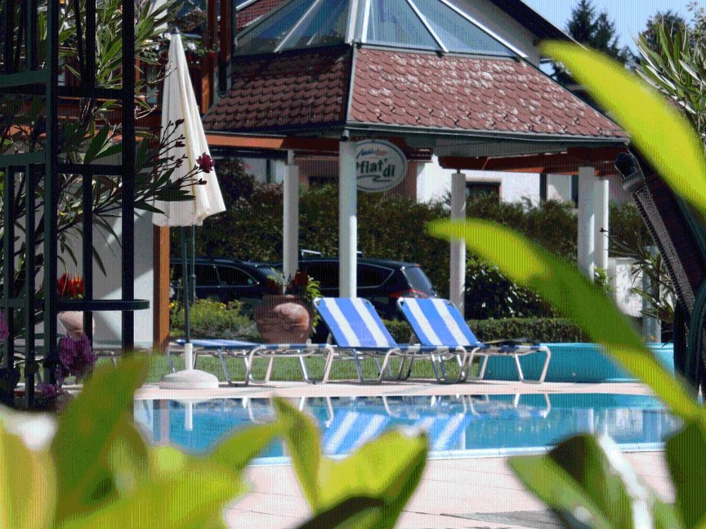 2 sillas y sombrilla junto a la piscina en Sportpension Aichholzer, en Oberaichwald