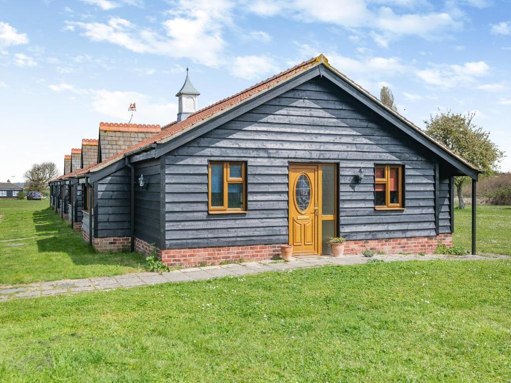 una piccola casa blu con una porta gialla in un campo di Orchard Cottage a Saint Osyth
