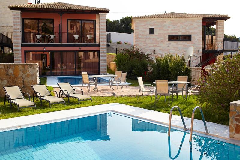 a pool with chairs and a table and a house at Ornella Beach Resort & Villas in Syvota