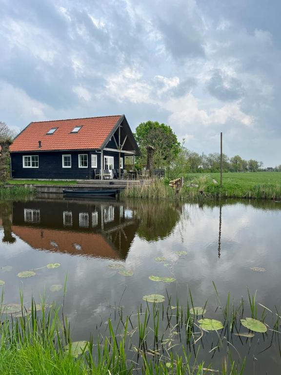 a house with a red roof sitting next to a lake at Vakantiehuisjes Marsherne in Poppingawier