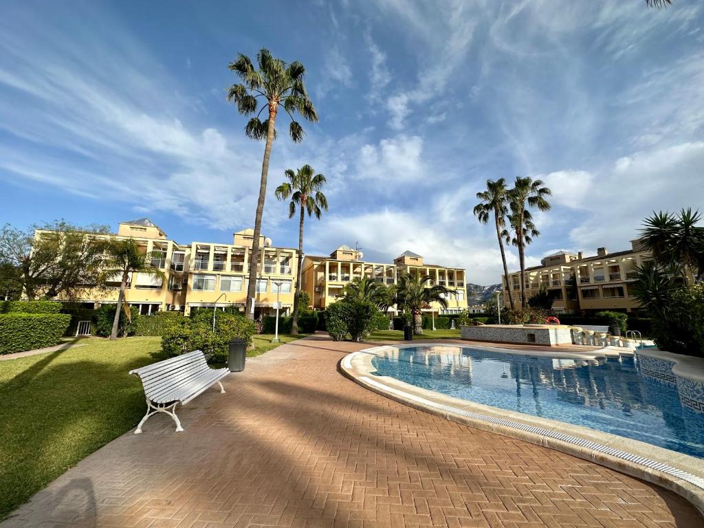 a resort swimming pool with a bench and palm trees at Las Delas in Denia