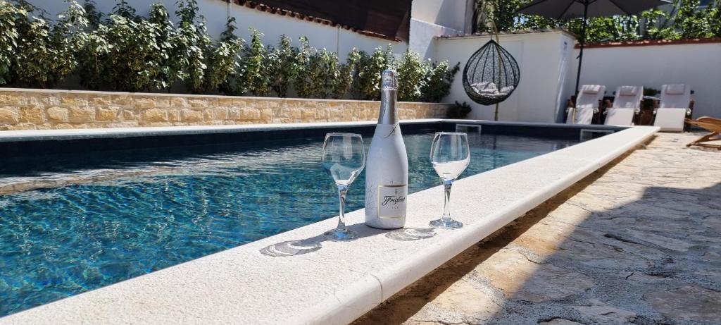 uma garrafa de vinho e dois copos de vinho ao lado de uma piscina em Villa Casa Mia em Privlaka