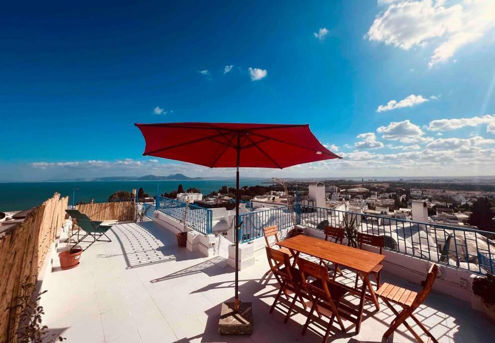 uma mesa e cadeiras numa varanda com um guarda-sol vermelho em The Blue Sea View Sidi Bou Said em Sidi Bou Saïd