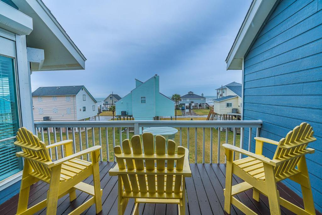 a balcony with two yellow chairs and a blue house at Hot Tub - Ocean Views - Steps to Private Beach - Quiet Location in Galveston