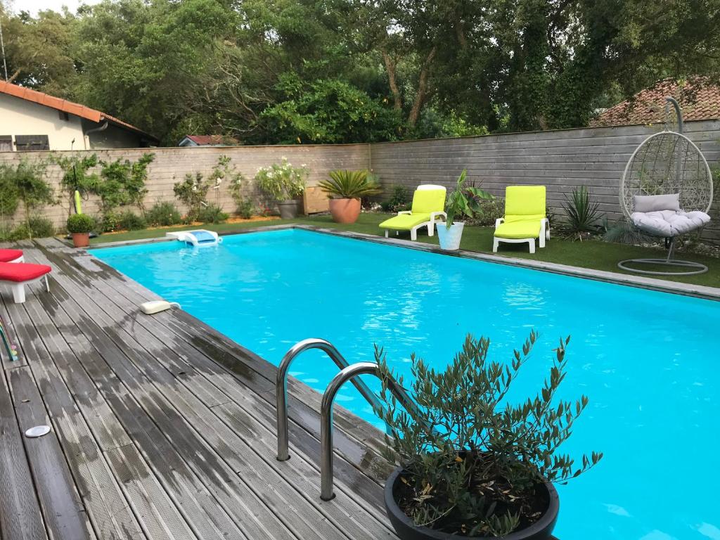 une piscine dans une cour arrière avec des chaises et une terrasse en bois dans l'établissement Maison avec piscine Labenne Océan, à Labenne