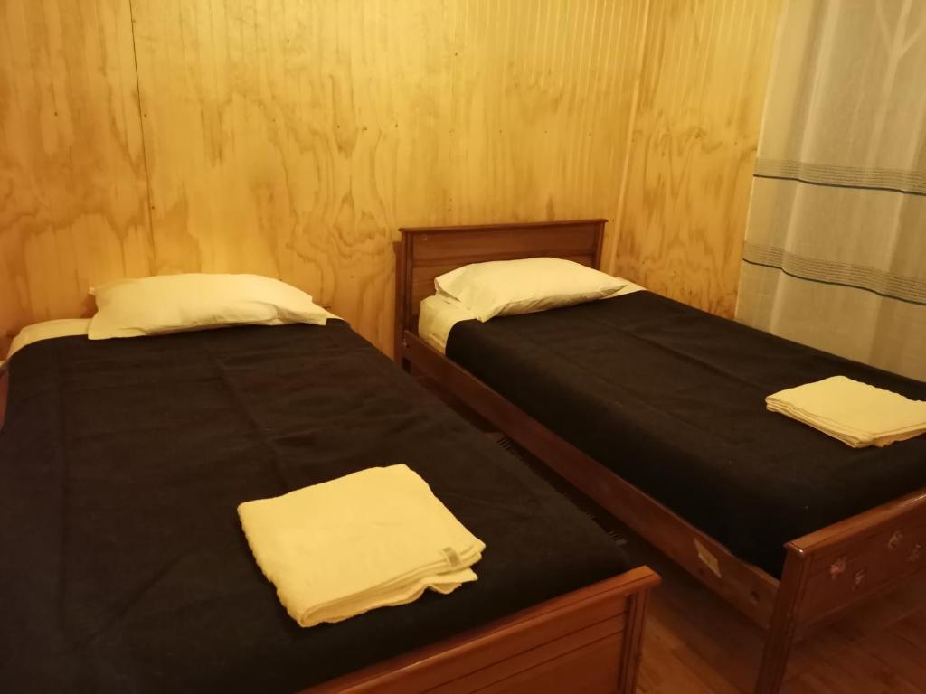 duas camas em um quarto com lençóis pretos e toalhas brancas em Cabañas Candelaria em Los Ángeles