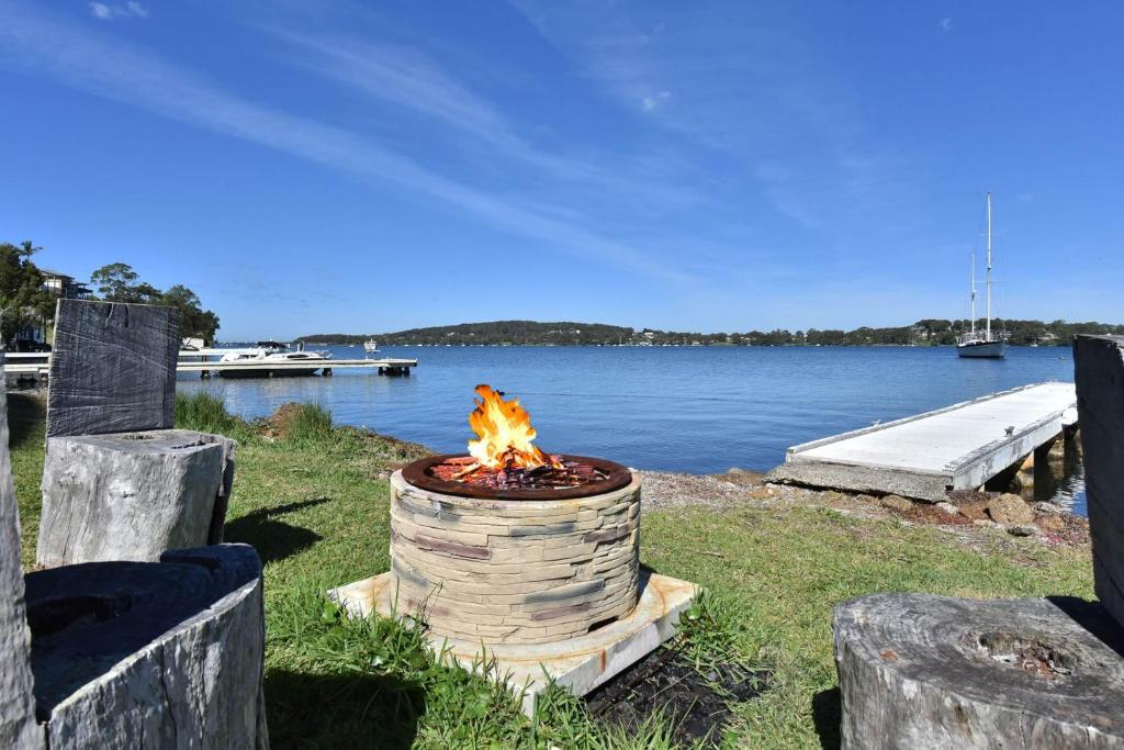 a fire pit in the grass next to a body of water at Water's Edge Apartment 2 absolute waterfront at Fishing Point on Lake Macquarie in Fishing Point