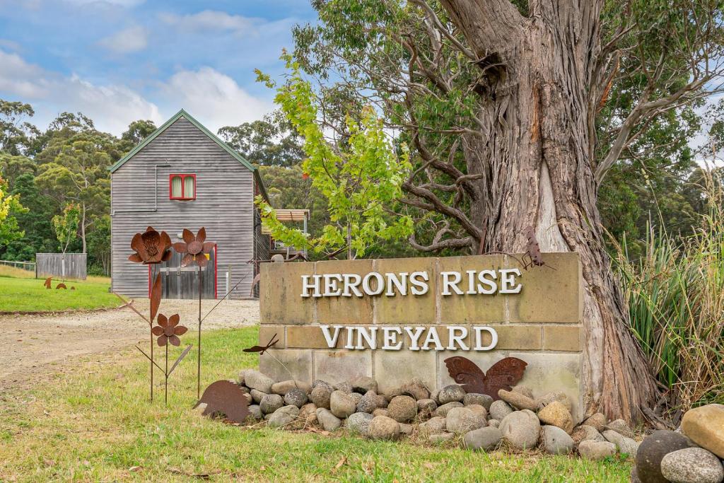 Un signo que lee garzas se eleva al viñedo junto a un árbol en Herons Rise Vineyard Accommodation, en Kettering