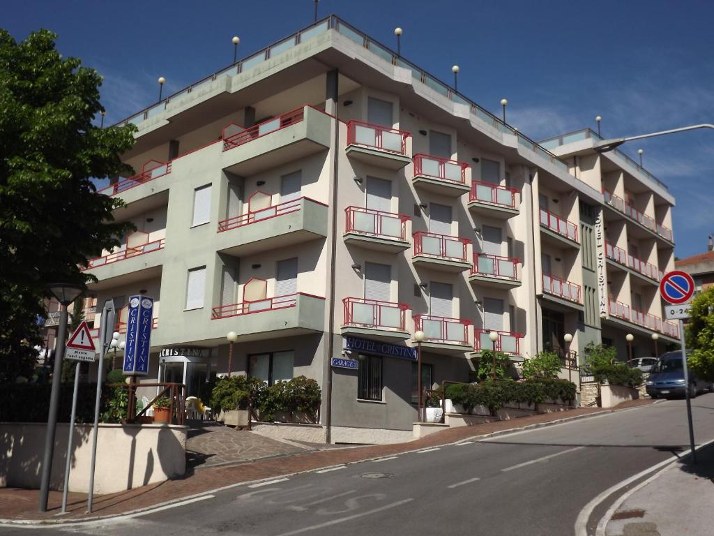 duży biały budynek z czerwonymi balkonami przy ulicy w obiekcie Hotel Cristina w mieście Chianciano Terme