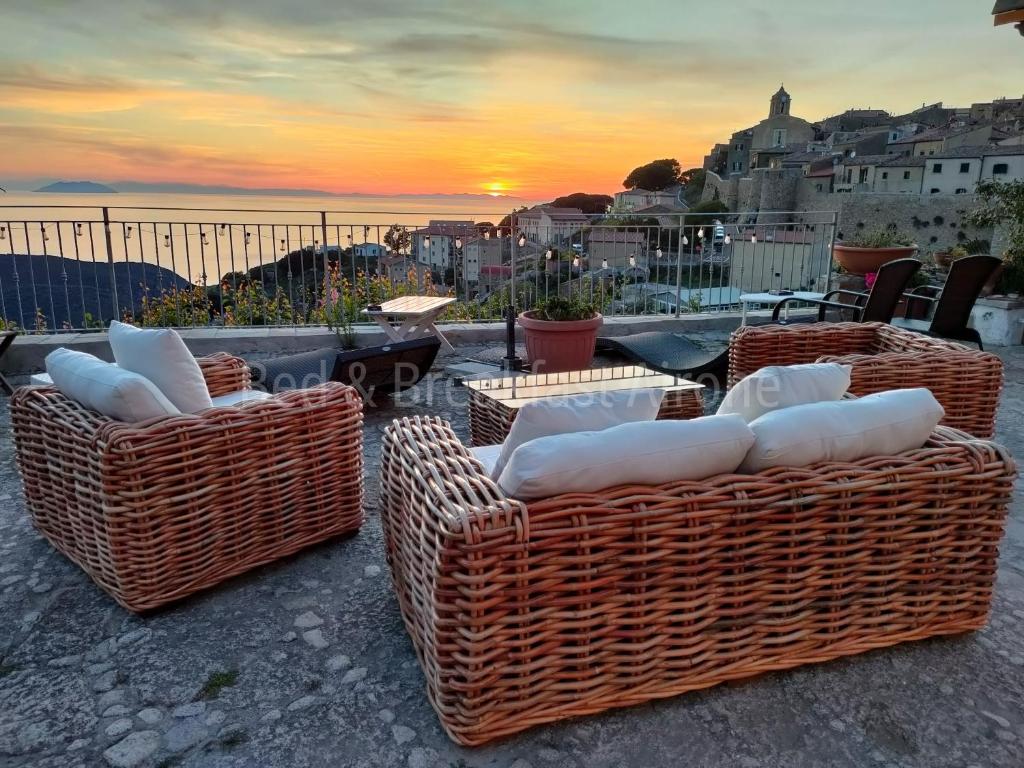four wicker chairs and tables with a sunset in the background at B&B Airone in Isola del Giglio