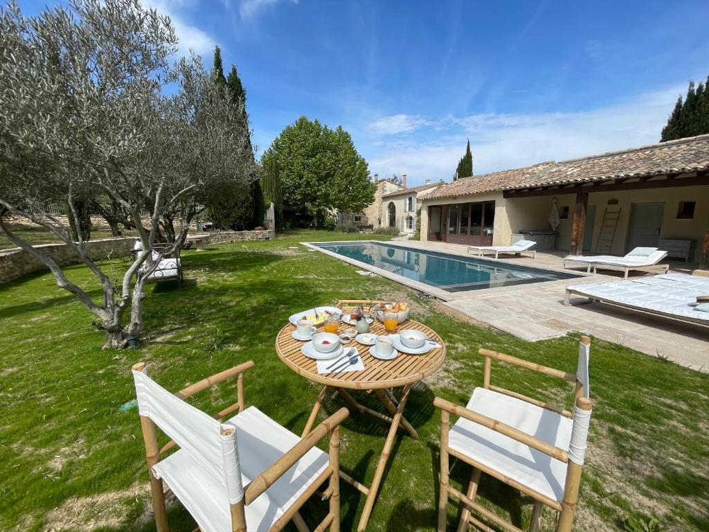 a table and chairs in a yard with a pool at MAS MILLÉSIME - Chambre double - petit déjeuner - piscine - Mas du XVIIIème siècle proche Saint-Rémy-de-Provence in Mas blanc des Alpilles