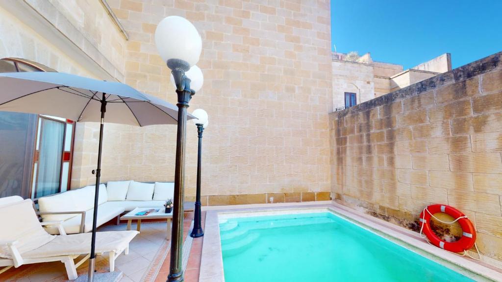 a swimming pool with an umbrella and white chairs at Qala Bed&Breakfast with swimming pool - IL-Wenniessa in Qala