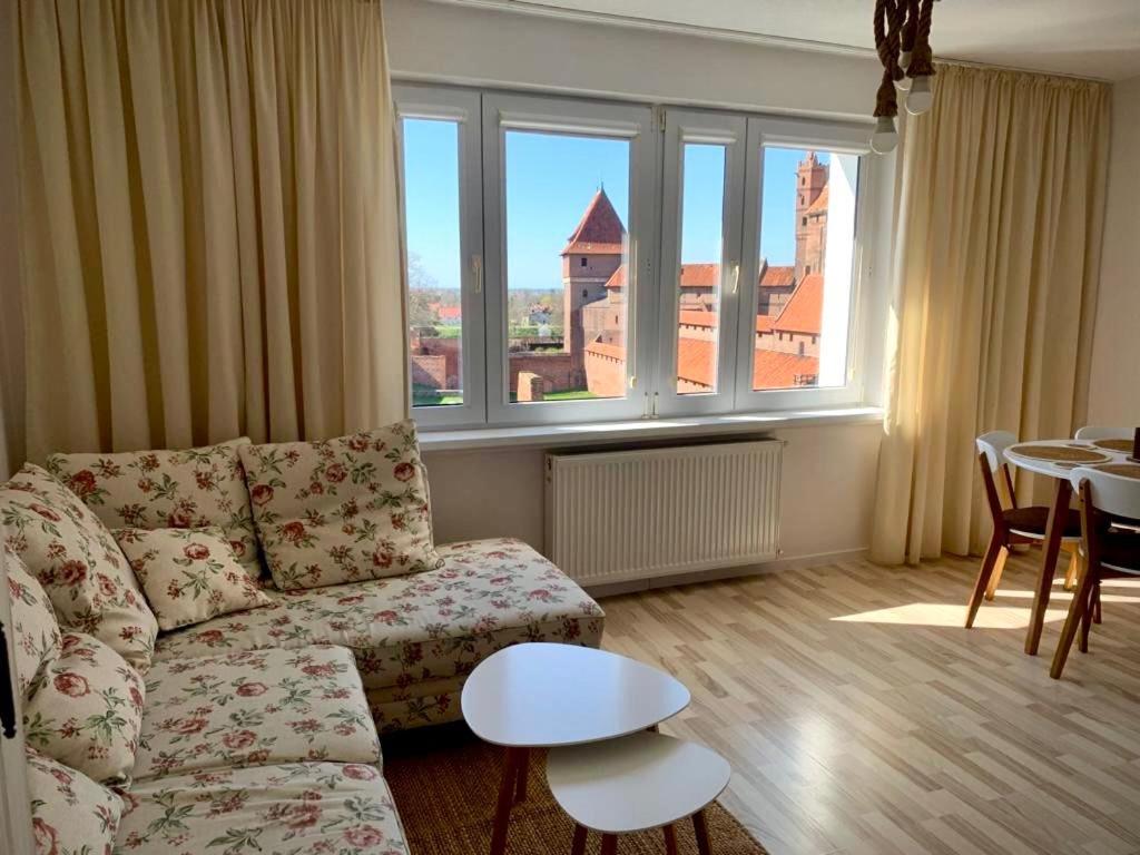 a living room with a couch and a table and windows at Widok Zamku o poranku in Malbork