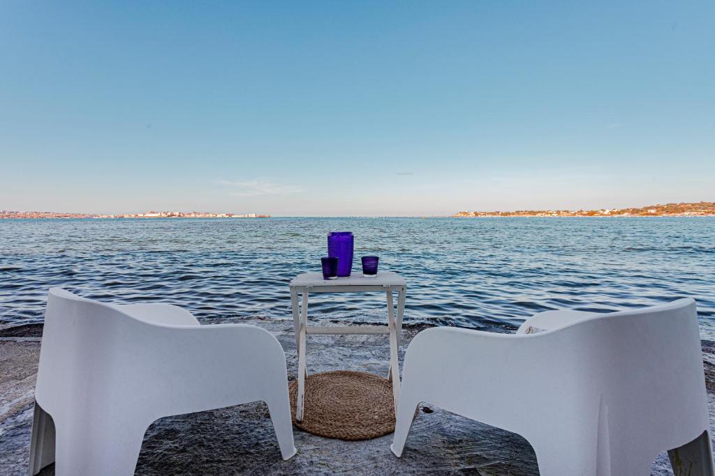 3 weiße Stühle und ein Tisch mit einem Getränk auf dem Wasser in der Unterkunft Villa Vivimar in Syrakus
