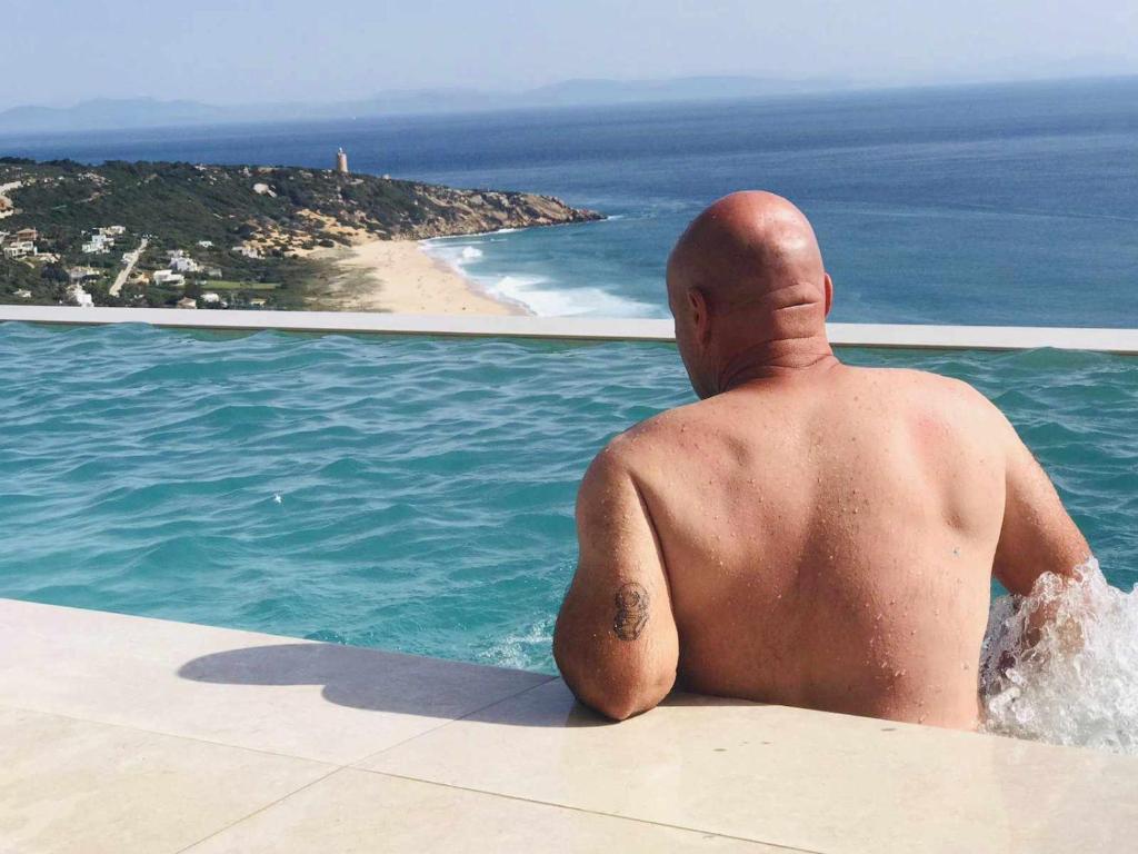 a man sitting on the edge of a pool looking at the ocean at Villa El Buzo in Zahara de los Atunes
