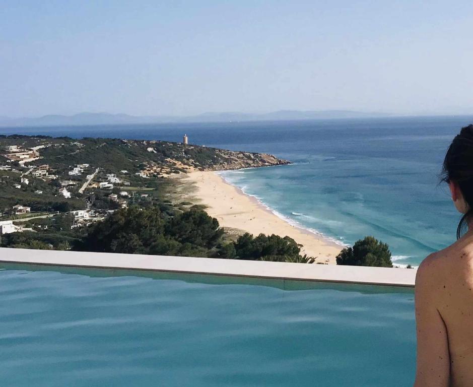 a woman standing on the edge of a swimming pool overlooking a beach at Villa El Buzo in Zahara de los Atunes
