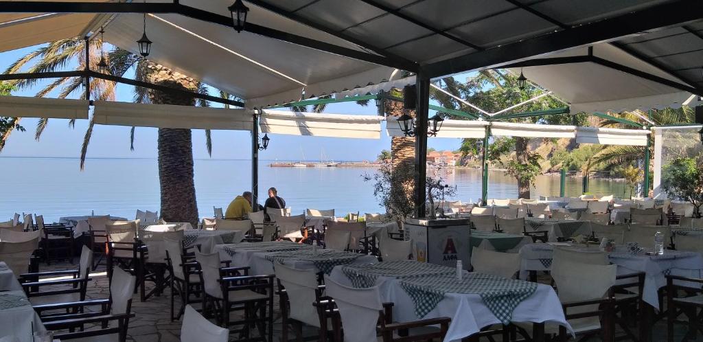 un ristorante con tavoli e sedie bianchi con vista sull'acqua di Triena Rooms a Mythimna