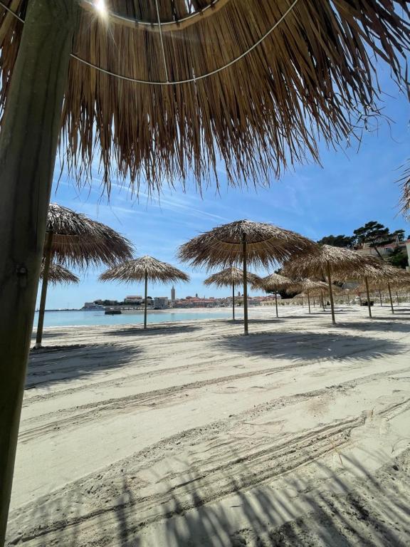 a beach with straw umbrellas and the ocean at Penthouse Damjan in Rab