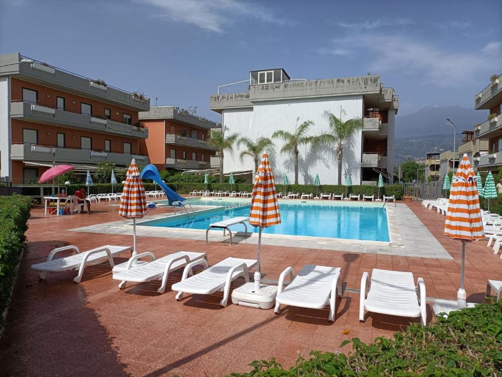 einen Pool mit Liegestühlen und Sonnenschirmen neben einem Hotel in der Unterkunft Blu Corallo in Mascali