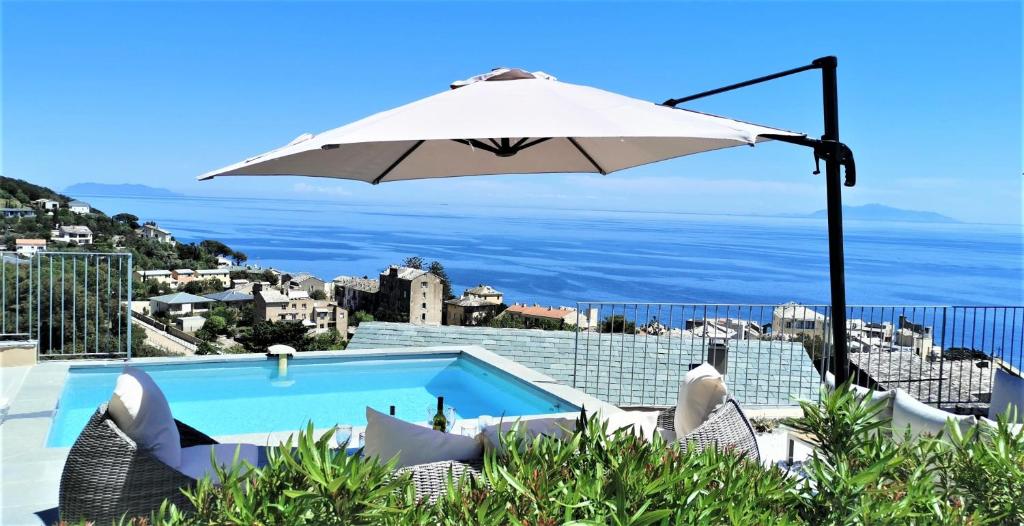 a pool with an umbrella and a view of the ocean at Villa Népita in Erbalunga