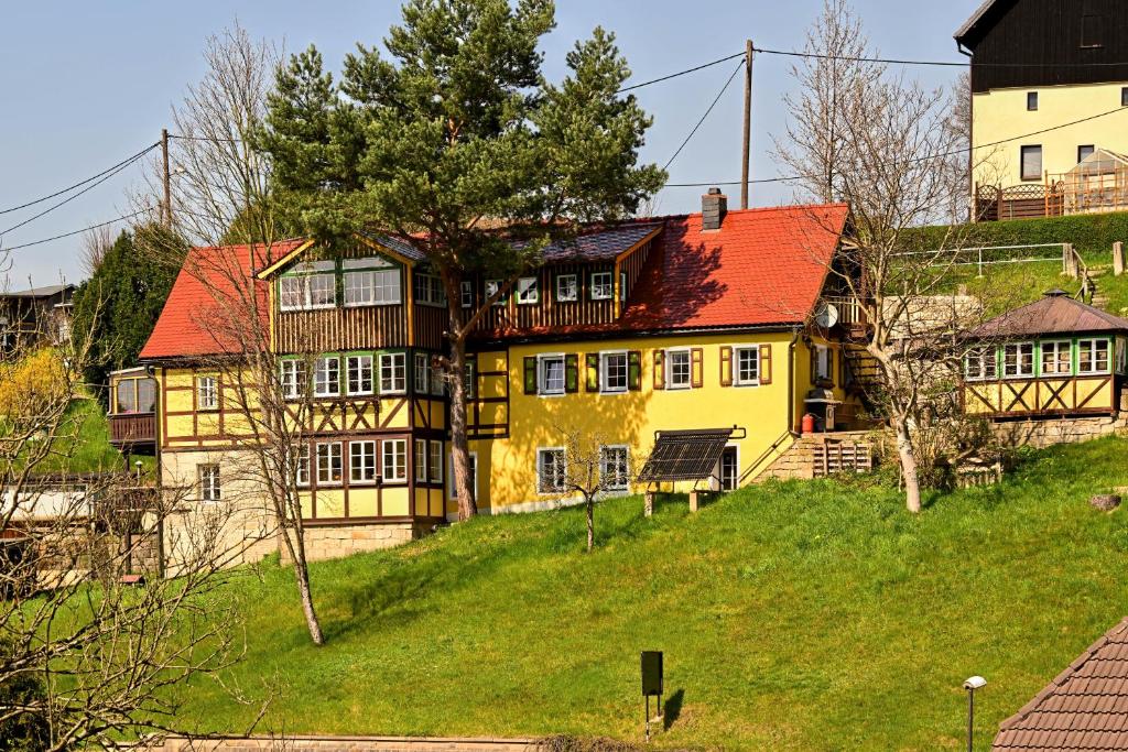 a yellow house with a red roof on a hill at Loft am Malerweg in Reinhardtsdorf