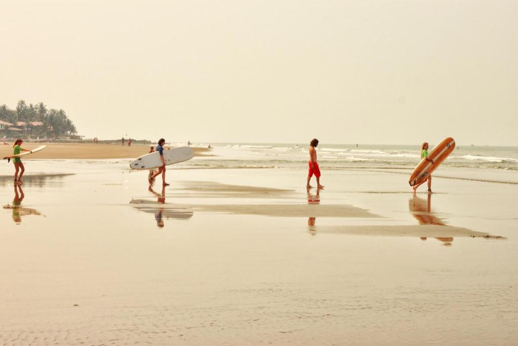 a group of people walking on the beach with surfboards at Beach Xaviers Guest House Colva in Colva