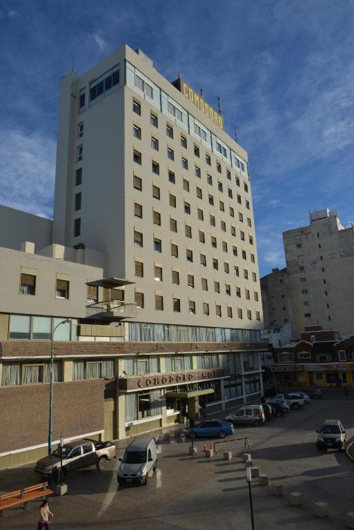 a large white building with cars parked in a parking lot at Comodoro Hotel in Comodoro Rivadavia