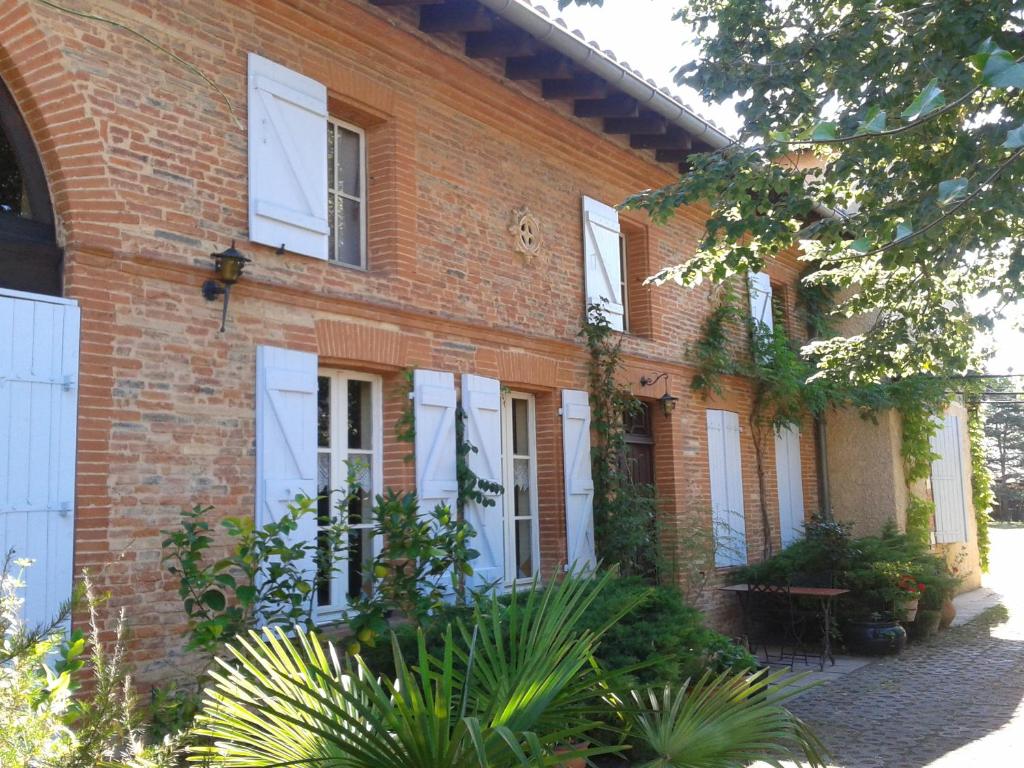 una casa de ladrillo con ventanas blancas con persianas y plantas en Ma Toulousaine Chambre d'Hôtes, en Toulouse
