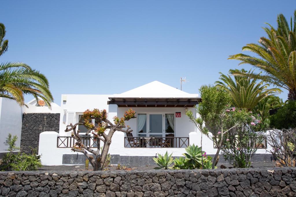 a white house with palm trees and a stone wall at Villa Isa sea views in Playa Blanca