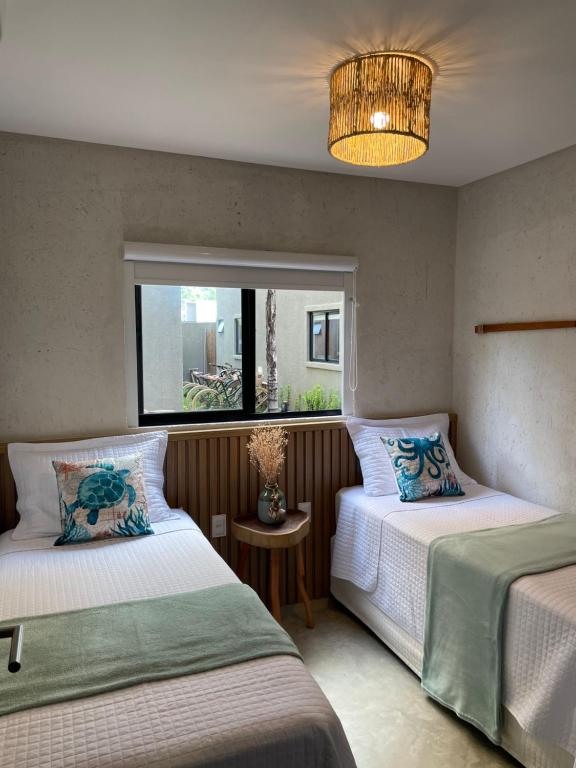 a bedroom with two beds and a window and a chandelier at MAKAI Milagres in São Miguel dos Milagres