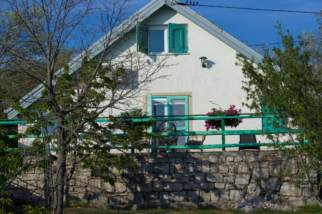 ein weißes Haus mit grünen Fenstern und einer Steinmauer in der Unterkunft Planinska kuća Agroturizam Kućica Mostar in Mostar