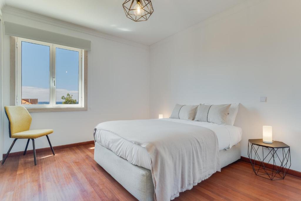 a white bedroom with a large bed and a chair at Bela São Tiago I in Funchal