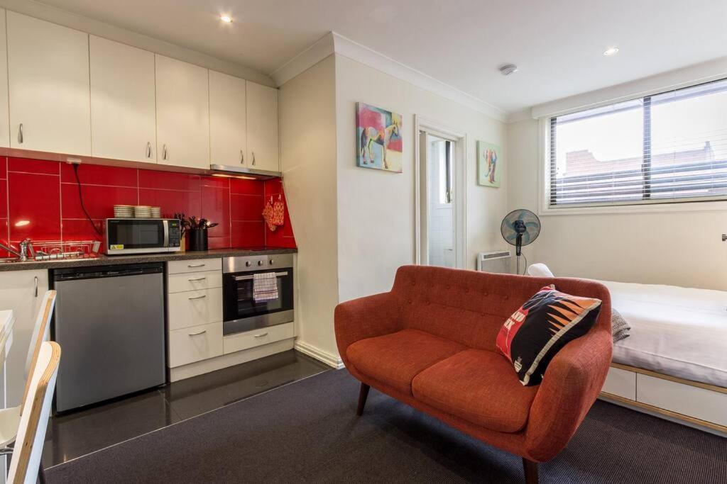 a living room with a red couch and a bed at Studio Apartment in the heart of Fitzroy in Melbourne