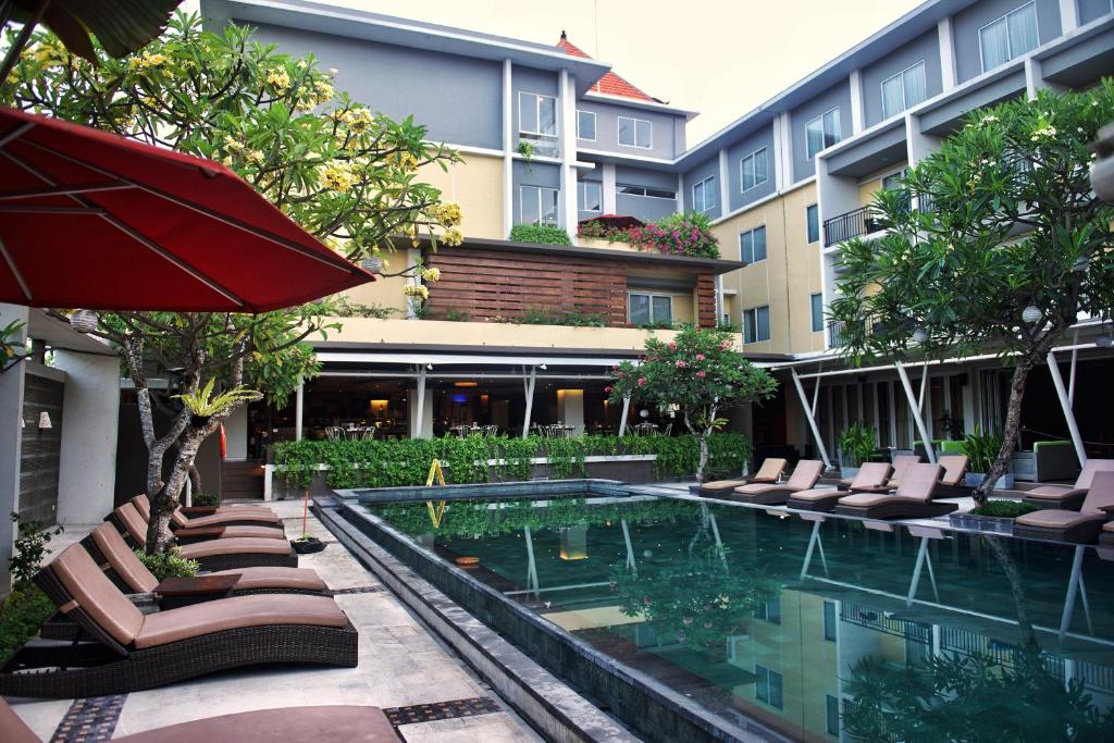 a hotel with a swimming pool with chairs and an umbrella at The Kana Kuta Hotel in Kuta