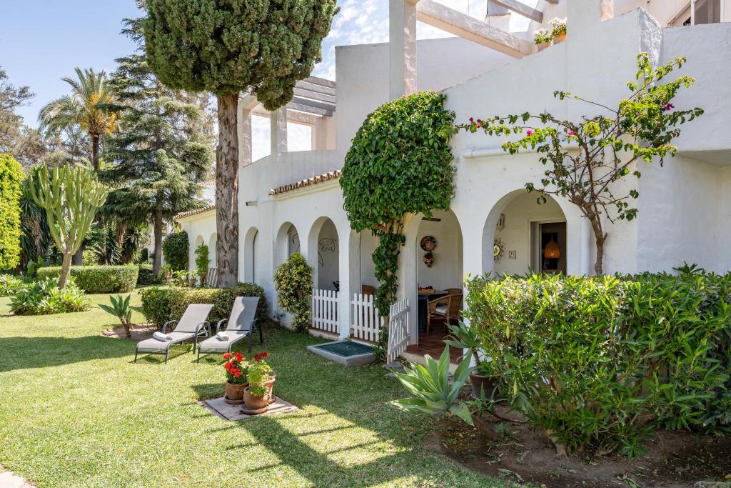 ein weißes Haus mit einem Garten mit Stühlen und Bäumen in der Unterkunft Casa Karma in Mijas