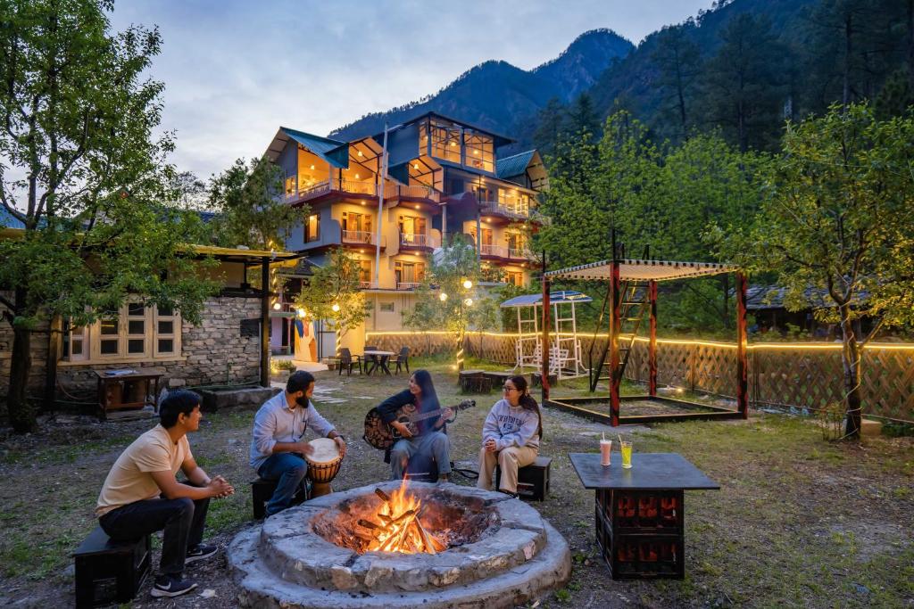 a group of people sitting around a fire pit in front of a house at Zostel Kasol (Katagla) in Kasol
