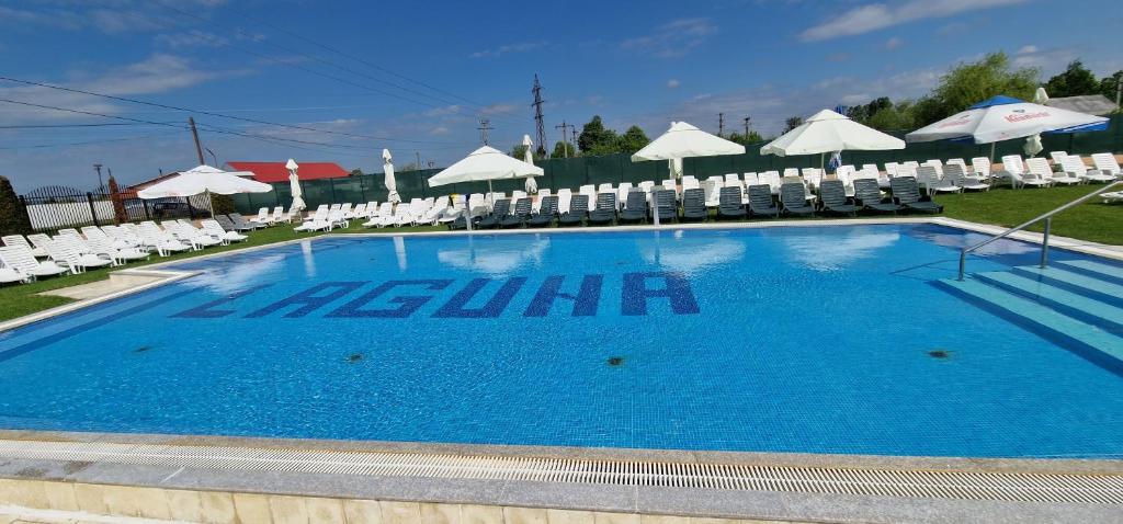 a large swimming pool with white chairs and umbrellas at Motel LAGUNA in Beiuş