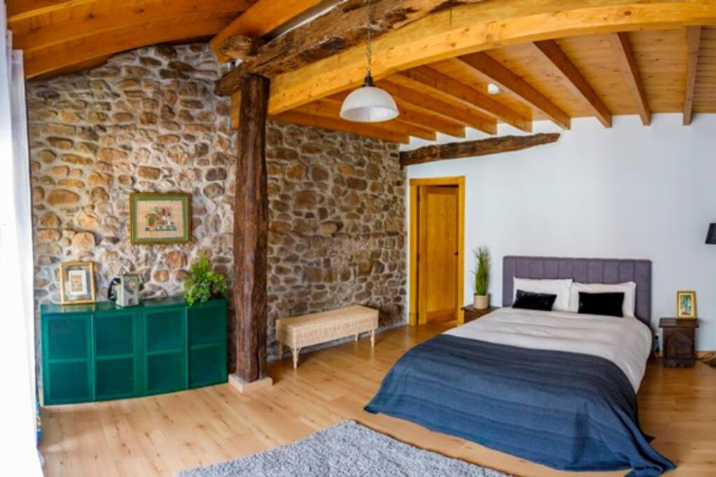 1 dormitorio con cama y pared de piedra en Casa el Envero, en Saro