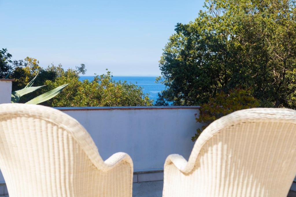 two wicker chairs sitting on a balcony with the ocean at Capo Bianco Studio by HelloElba in Portoferraio