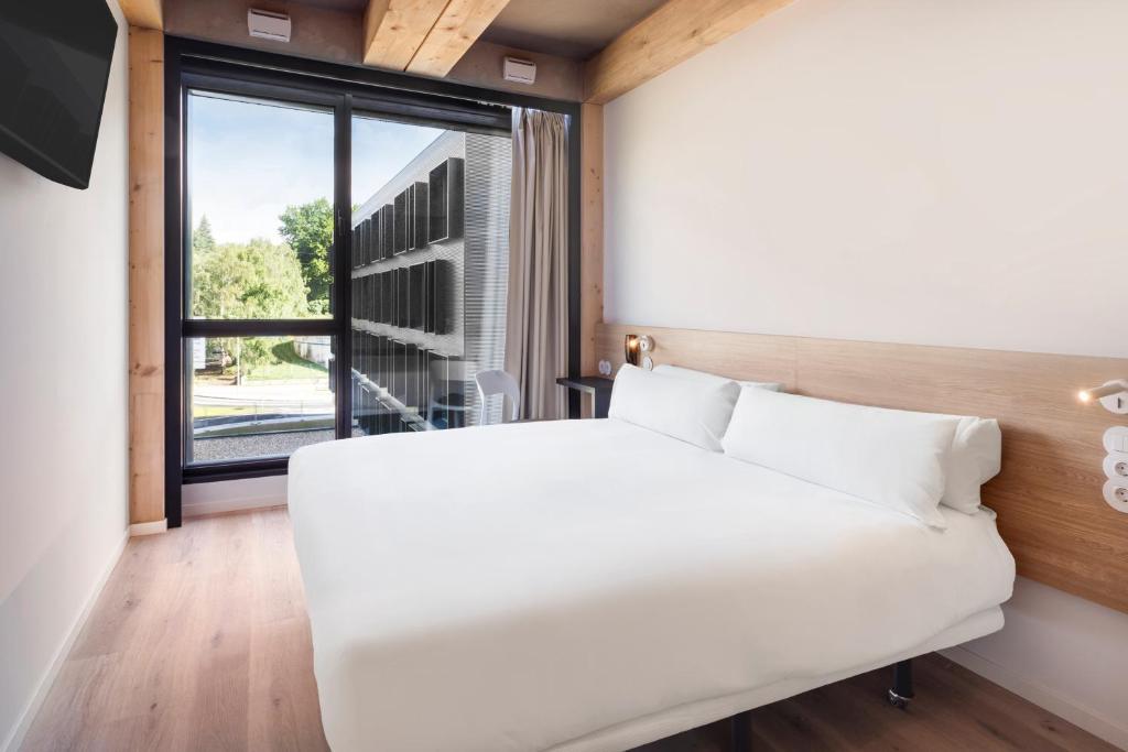 a white bed in a room with a large window at B&B HOTEL Guimarães in Guimarães