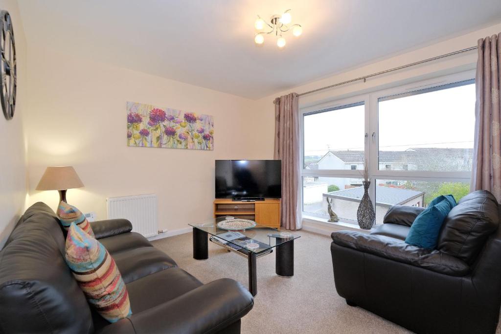 sala de estar con muebles de cuero y ventana grande en Caledonia Newhills Apartment en Aberdeen