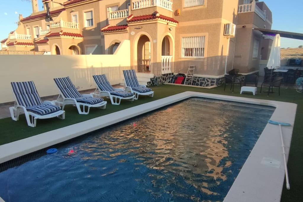 una piscina di fronte a un edificio con sedie e una casa di adosado con piscina a 10 minutos de Alicante ad Alicante