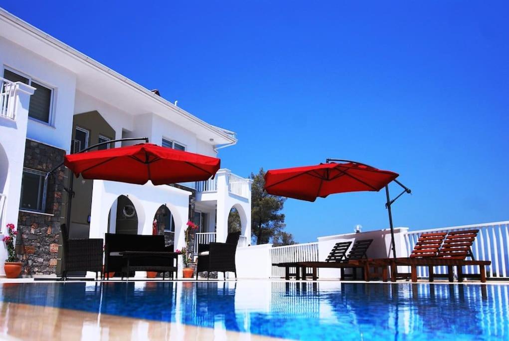 two red umbrellas and chairs next to a swimming pool at The Royal Links two bedroom apartment in Ortaca