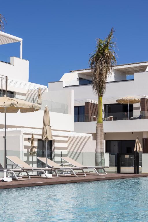 a pool with umbrellas and a palm tree next to a building at Esmeralda Cotillo Homes by LIVVO in El Cotillo