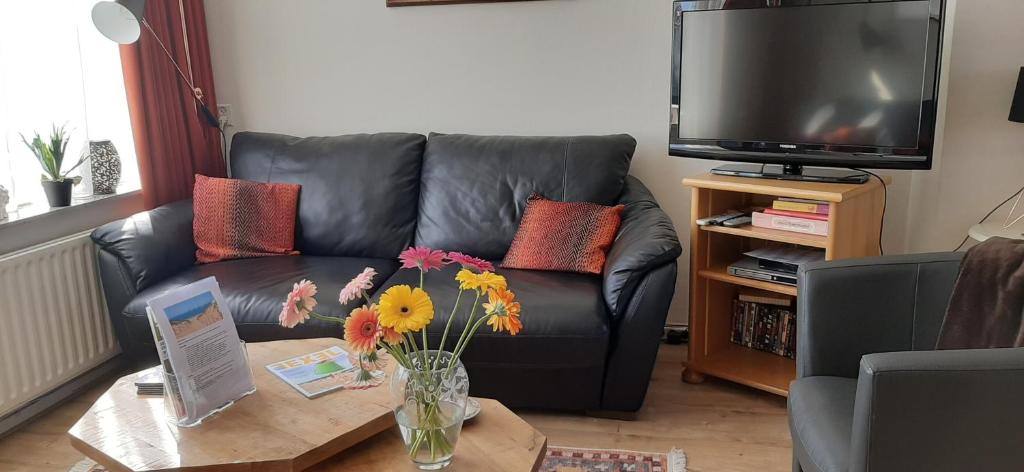 a living room with a leather couch and a table with flowers at Logies Plevierstraat in De Koog