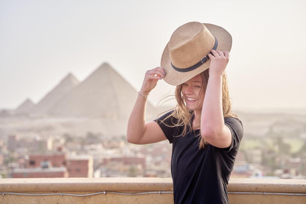 Gardenia Apartment Pyramids View في القاهرة: امرأة ترتدي قبعة راعي بقر أمام الاهرامات