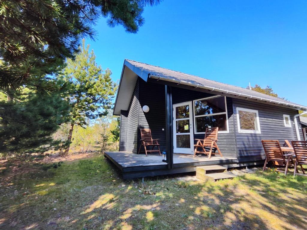 una pequeña casa con mecedoras en el porche en Tranum Klit Camping og Hytteudlejning, en Brovst